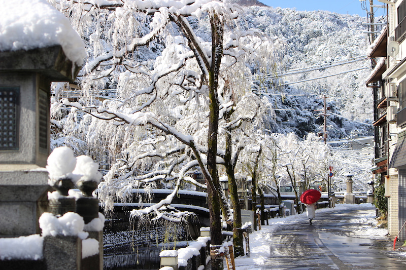 雪に包まれた冬の城崎温泉と柳並木を歩く浴衣姿の人