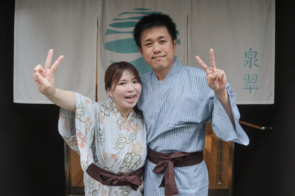 城崎温泉 泉翠へマタニティ旅行で訪れ、旅館の暖簾の前でゆかた姿でピースサインをするご夫婦
