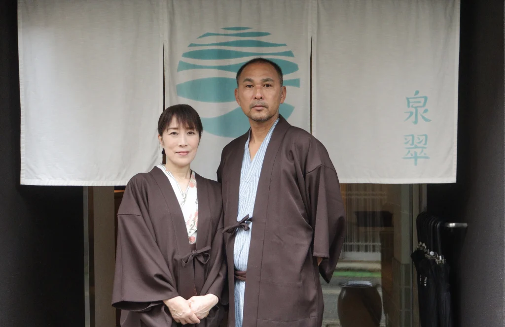 結婚30周年の記念日旅行で城崎温泉 泉翠を訪れ、旅館の暖簾の前で並んで記念撮影するご夫婦